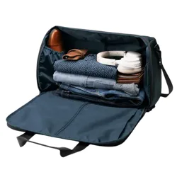 A duffel bag with a removable shoe compartment, holding a pair of brown shoes, rolled shirts, jeans, and accessories. Includes a detachable shoulder strap.