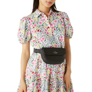 A black leather belt bag with the Kate Spade logo in the center, featuring a sleek rectangular shape and an adjustable black strap.