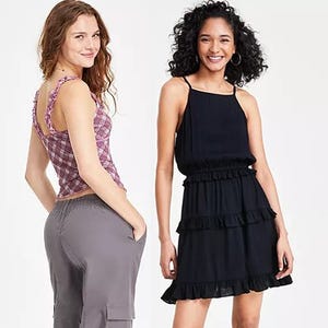Two women modeling clothing, one in a pink patterned sleeveless top and grey pants, and the other in a sleeveless black tiered dress.