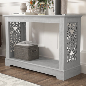A gray console table with intricate decorative side panels, featuring books and a vase on top, and a woven basket with folded towels on the lower shelf.