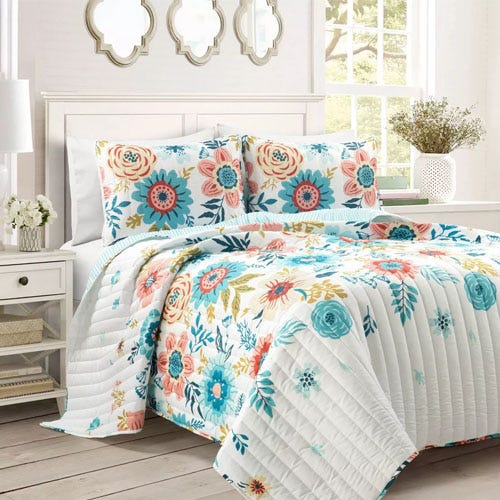 A floral patterned quilt and pillowcases set on a bed with a white headboard, flanked by white nightstands and mirrors.