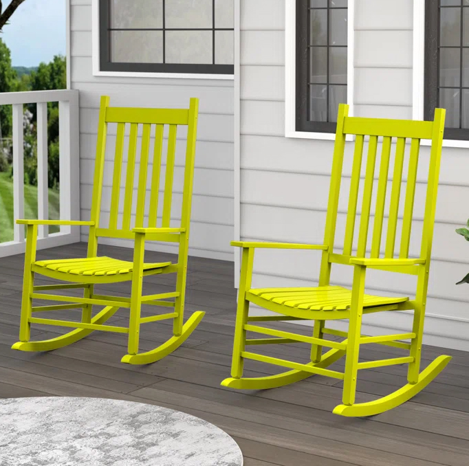 Two lime green wooden rocking chairs are placed on a porch with a gray wooden floor, near white siding and windows.