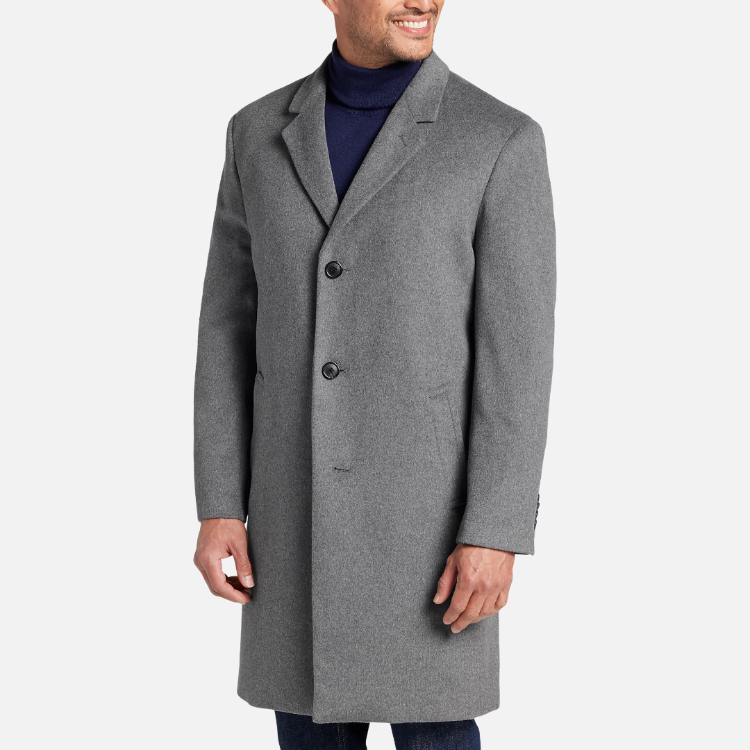 A man wearing a gray overcoat and a navy turtleneck sweater.