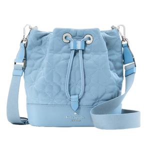 Light blue quilted bucket bag with a floral pattern, featuring a drawstring closure, adjustable shoulder strap, and silver hardware. Brand name and logo embossed on the front.