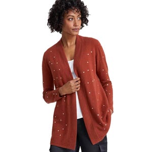 Rust-colored cardigan with white polka dots, featuring an open front design. It's worn over a white top and black pants.