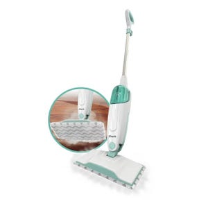 A white and green Shark brand steam mop with a rectangular cleaning pad at the bottom. A zoom-in circle shows the steam feature on a hardwood floor.
