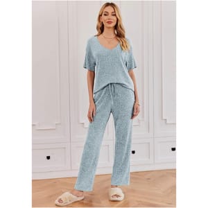 A woman models a light blue knit loungewear set with fuzzy slippers.