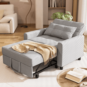 A gray pull-out chair bed with a throw blanket is set in a modern living room. There's an open book on a small round table nearby, surrounded by neutral decor.