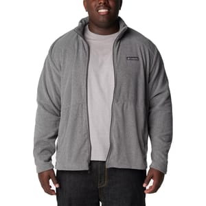 A man wears a Columbia Castle Dale Big Fleece in light gray, featuring a full zip front, high collar, and brand logo on the chest, paired with a gray T-shirt and dark jeans.