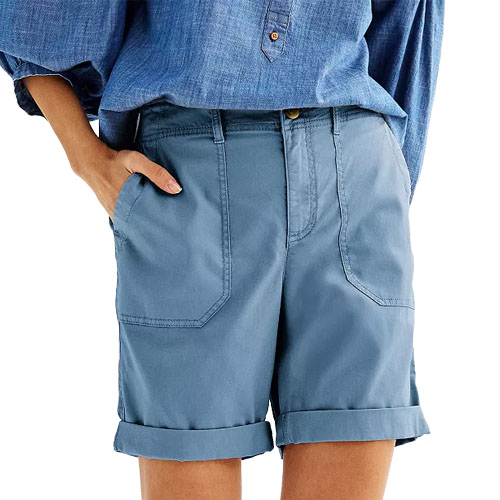 A person wearing cuffed blue shorts with large front pockets and a blue button-down shirt.