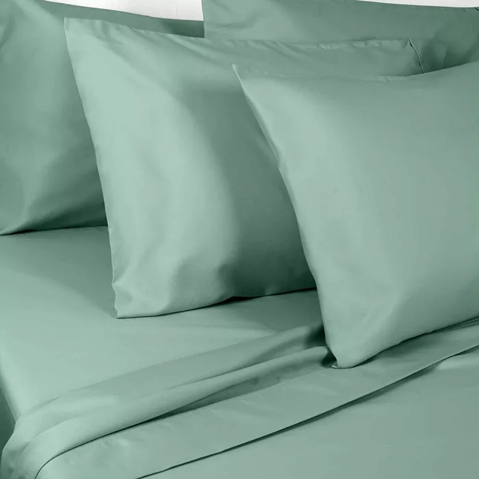 A set of light green bedsheets, including pillowcases and a flat sheet, displayed on a bed.