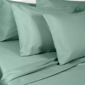 A set of light green bedsheets, including pillowcases and a flat sheet, displayed on a bed.