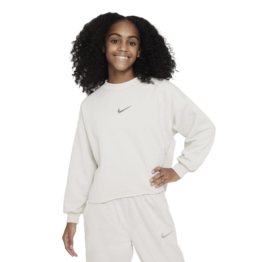 The Nike Girls' Fleece features a soft, cream-colored sweatshirt with the Nike logo on the chest, paired with matching pants also displaying the logo.