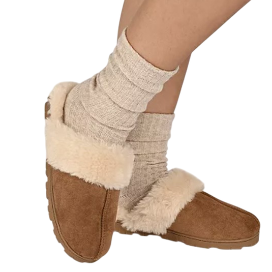 Cozy slippers with a fluffy fur lining and brown suede exterior are worn with thick, beige socks.