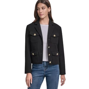 A woman is wearing a black tailored jacket with gold buttons, featuring two chest pockets and two lower pockets. She pairs it with a gray top and blue jeans.