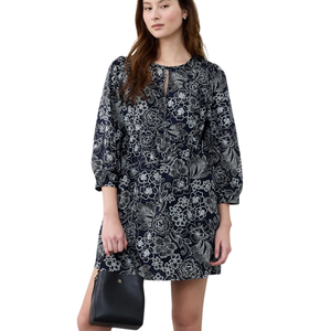 A woman is wearing a dark floral-patterned dress with long sleeves and a keyhole neckline, holding a black handbag.