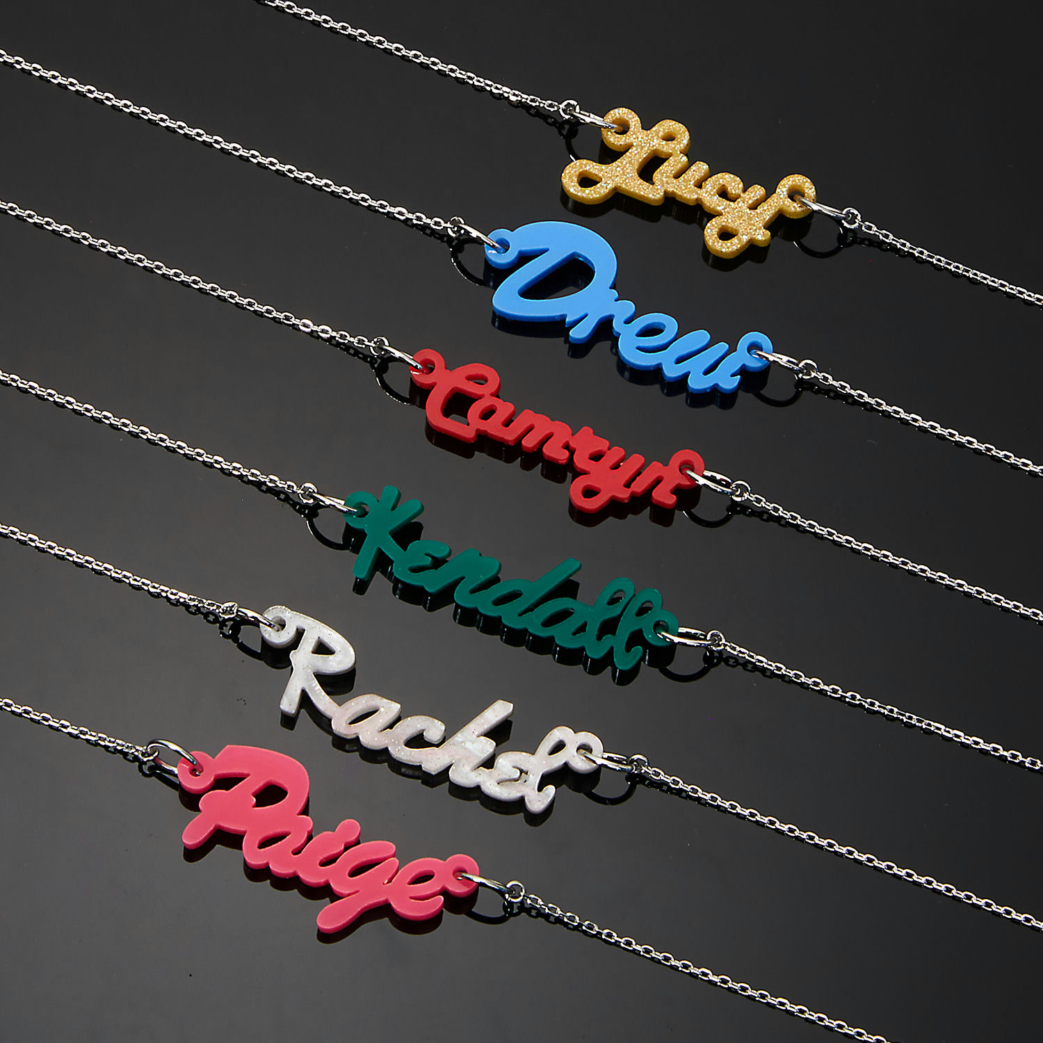 Personalized name necklaces in different colors displayed on a dark background.