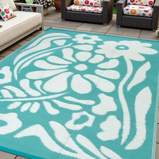 Outdoor patio with rattan furniture features vibrant floral cushions and a large rectangular outdoor rug with a teal and white floral design.