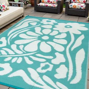 Outdoor patio with rattan furniture features vibrant floral cushions and a large rectangular outdoor rug with a teal and white floral design.