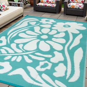 Outdoor patio with rattan furniture features vibrant floral cushions and a large rectangular outdoor rug with a teal and white floral design.