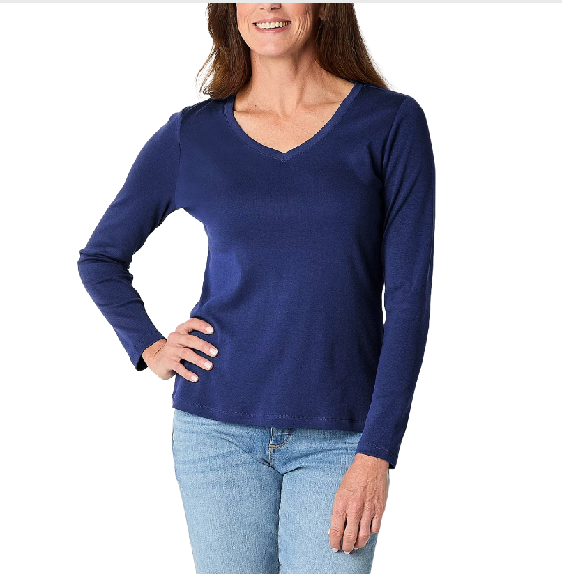 A woman wearing a long-sleeve, navy blue V-neck top paired with light blue jeans is shown standing with one hand on her hip.
