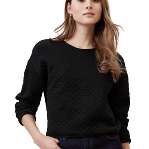 A woman is wearing a black quilted Banana Republic Factory sweater with long sleeves and a crew neckline, paired with dark jeans.