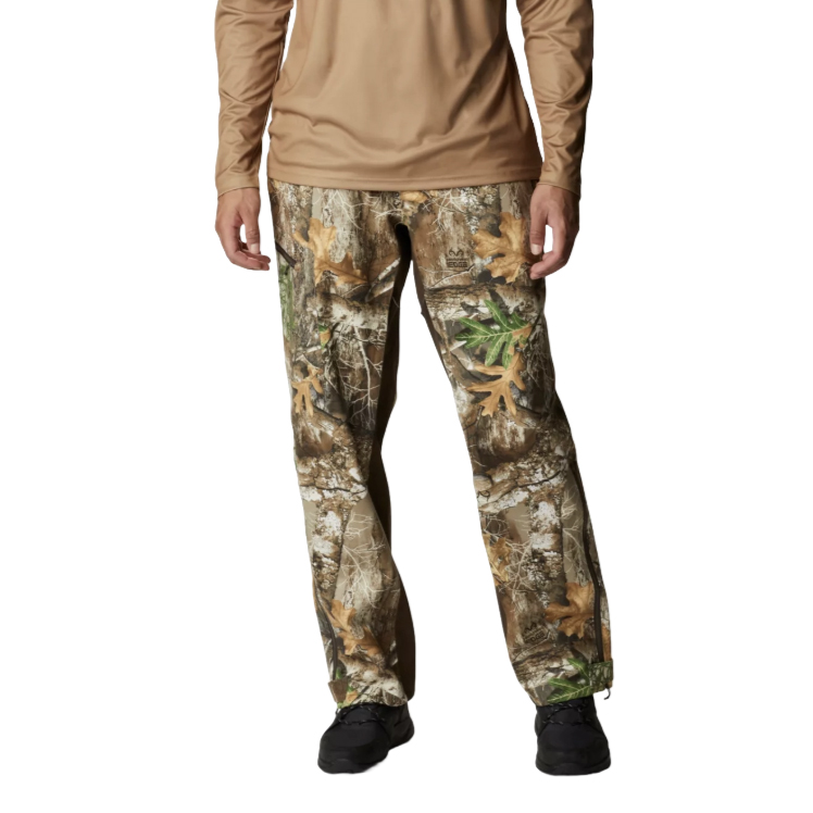 A person wearing camouflage pants with a nature pattern featuring leaves and branches, paired with a plain brown long-sleeve shirt and black footwear.