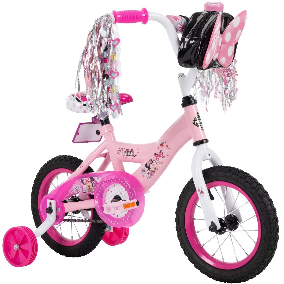 A pink and white children's bicycle with training wheels features a Minnie Mouse theme, pink handlebars with tassels, and a small backpack attached to the handlebar.