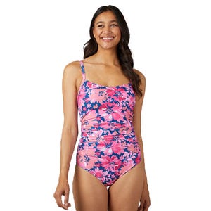 A woman is wearing a pink floral one-piece swimsuit with adjustable straps and ruched detailing around the waist.
