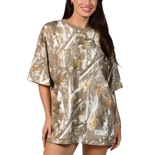 A woman is wearing an oversized camouflage-patterned t-shirt featuring a mix of brown, white, and green tones.
