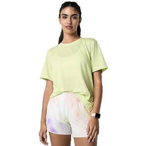 A woman is wearing a light yellow T-shirt and white shorts with a subtle multicolor design. She has a smartwatch on her wrist.