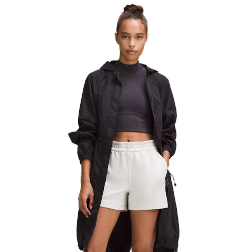 A woman is wearing a black hooded jacket, a dark cropped top, and light-colored shorts.