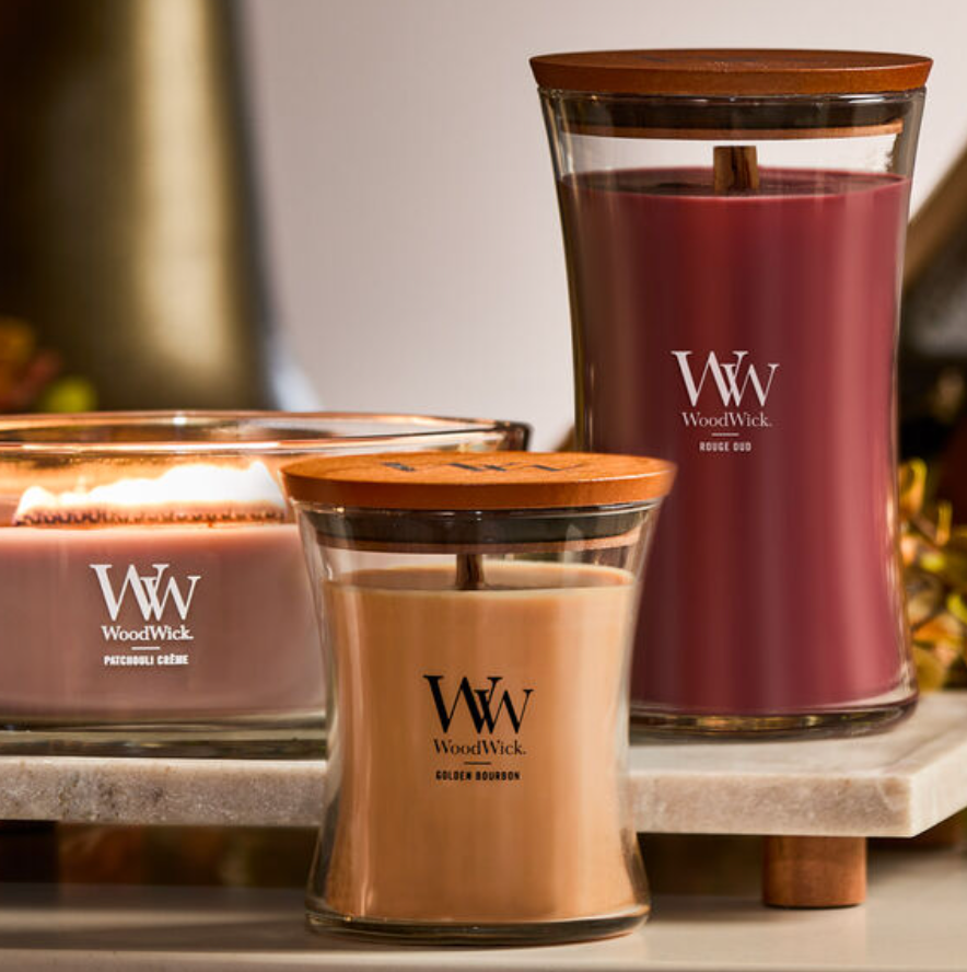 Three WoodWick candles with wooden lids: Patchouli Crème, Golden Bourbon, and Rouge Oud.