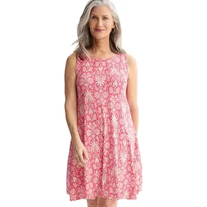 A woman is wearing a sleeveless, knee-length dress with a red floral pattern on a white background.