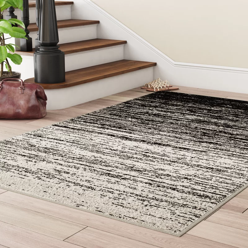 A black and white gradient area rug is placed on a hardwood floor near a staircase with wooden steps and a dark railing.