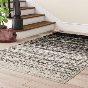 A black and white gradient area rug is placed on a hardwood floor near a staircase with wooden steps and a dark railing.