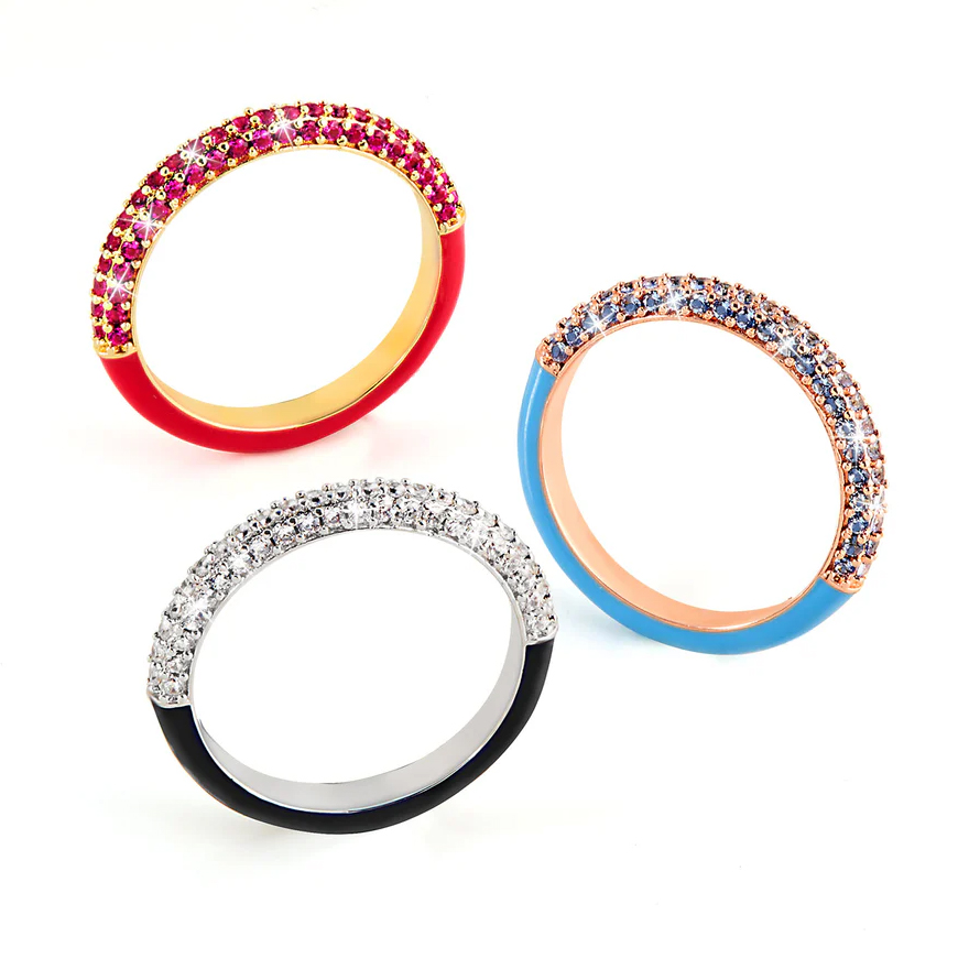 Three stackable rings, each featuring a gold, rose gold, or silver band with colored enamel and pave-set stones. The rings are red with rubies, blue with sapphires, and black with clear crystals.