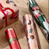 The photo shows various rolls of festive wrapping paper featuring diverse characters and Christmas-themed designs, alongside a wrapped gift box with a red ribbon.