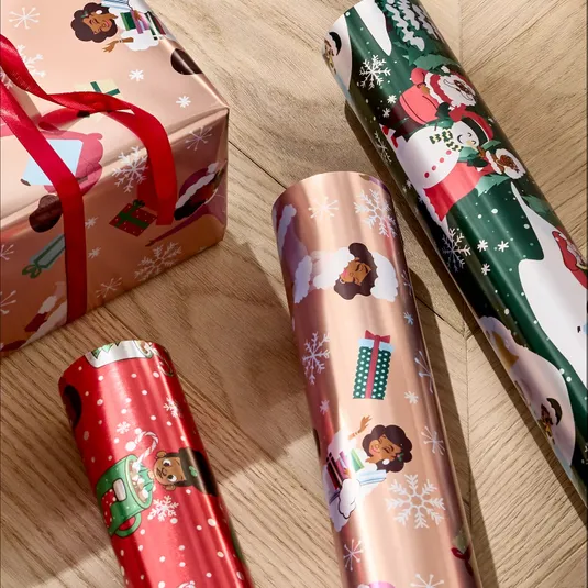 The photo shows various rolls of festive wrapping paper featuring diverse characters and Christmas-themed designs, alongside a wrapped gift box with a red ribbon.