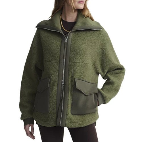 A woman is wearing an olive green fleece jacket with a zipper and large pockets, paired with dark pants.