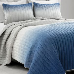 A plush quilt set with ombre blue-to-gray tones, featuring textured horizontal stitching. Includes a king-size quilt and two matching pillow shams, providing a cozy and stylish bedding option.