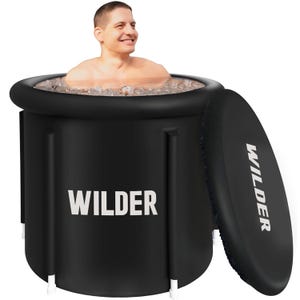 A black Cold Plunge Tub labeled \“WILDER\“ with an open top, filled with ice and a person inside. A matching lid with the same label is positioned beside it.