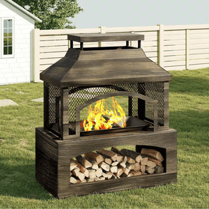 A wood-burning outdoor fireplace with a mesh screen and storage space for logs underneath is shown in a grassy yard with a wooden fence and white house in the background.