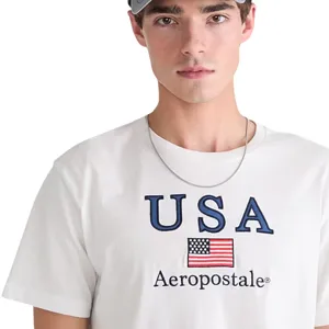 A person is wearing a white Aeropostale t-shirt with \“USA\“ and an American flag, along with a silver necklace and a gray cap.