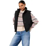 A woman is wearing a black puffer vest over a multicolored patterned sweater paired with blue jeans.