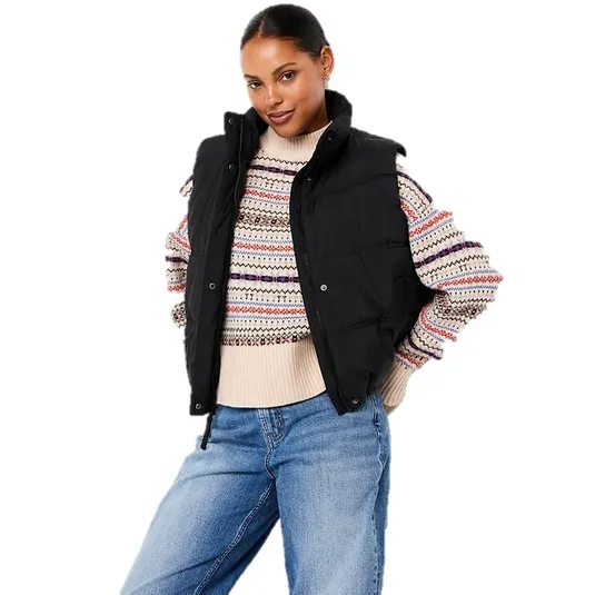 A woman is wearing a black puffer vest over a multicolored patterned sweater paired with blue jeans.