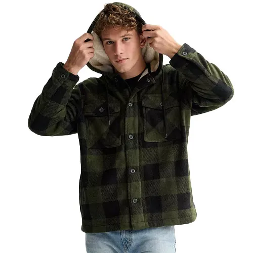 A man wears a green and black plaid hooded jacket with buttoned chest pockets and light blue jeans.