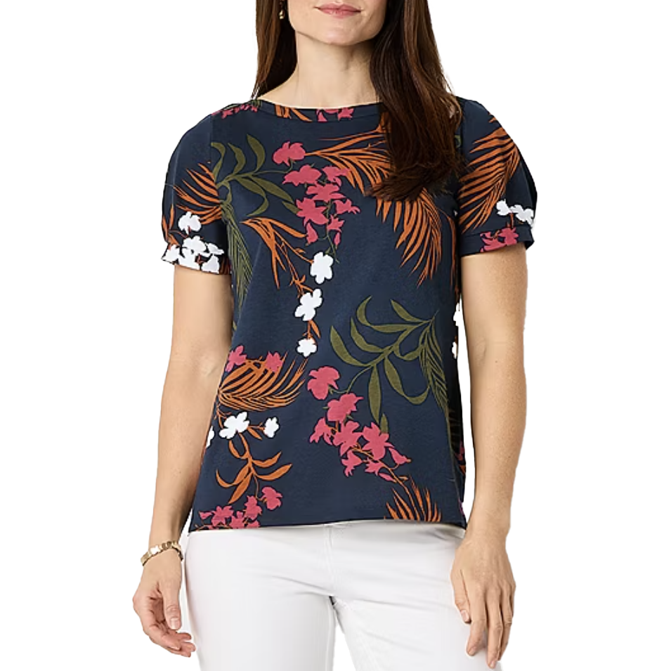 A woman is wearing a navy blue blouse with a floral print in pink, orange, white, and green, paired with white pants.