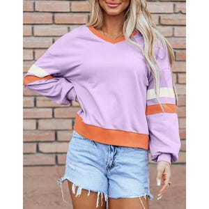A woman wearing a purple V-neck sweatshirt with striped sleeves and light blue denim shorts.