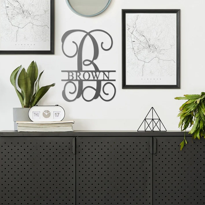 A wall-mounted personalized family name sign, houseplants, framed maps, a round mirror, a digital desk clock, and a geometric-shaped tabletop ornament.